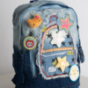 JINZU is a stylish medium-sized denim backpack adorned with playful, colorful pins—perfect for adding whimsy to your look. Lightweight and well-compartmentalized, it keeps your essentials organized whether you're heading to class or a casual party.