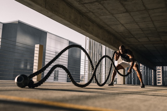 A male athlete performing a high-intensity rope workout in an industrial urban setting, representing the durability needed for a gym fitness backpack.